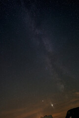 Milky Way in front of the blue night sky, the planet Jupiter can be seen, vehicel parts of two...