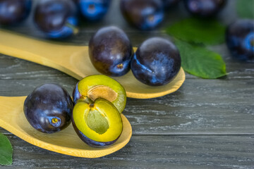 ripe fresh plums close-up. plum halves in wooden spoons on a wooden background. plum crop.