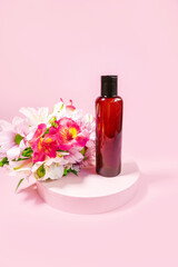 Obraz na płótnie Canvas Dark glass cosmetic bottle on pink background decorated with flowers. Presentation poster. Banner with place for text. Space for text. Mock up of cosmetic product. Shampoo, massage oil. Aromatherapy