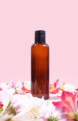 Obraz na płótnie Canvas Dark glass cosmetic bottle on pink background decorated with flowers. Presentation poster. Banner with place for text. Space for text. Mock up of cosmetic product. Shampoo, massage oil. Aromatherapy