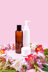 Fototapeta na wymiar Set of cosmetic products on pink background decorated with flowers. Presentation poster. Banner with text. Space for text. Mock up of cosmetic product. Dispenser bottle, jar of cream,dark glass bottle