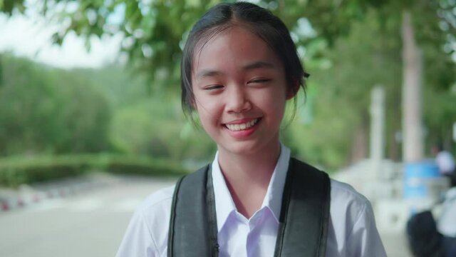A smiling Asian female student in a white high school uniform is standing on the side of the road waiting for cars to go home after school.