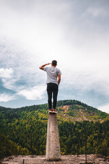 Vertical shot of a young male standing on a platform surrounded by hills under a cloudy sky © Vlad Chețan/Wirestock