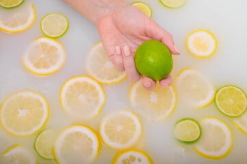 Close-up of a female hand holding a lime over white water with lemon slices