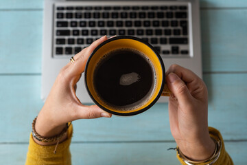 Close up of a woman's hands holding a cup with coffee on a laptop Concept of working at home