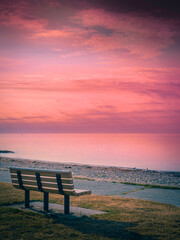 Fototapeta na wymiar Tranquil Pink Twilight Seascape and Dramatic Cloudscape over the Bench on Cape Cod Beach