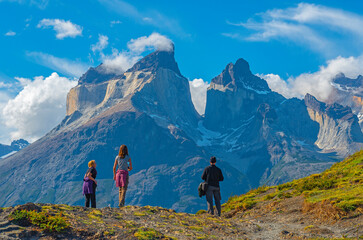 A group of three tourists looking upon the Andes peaks of Cuernos del Paine in Chilean Patagonia....