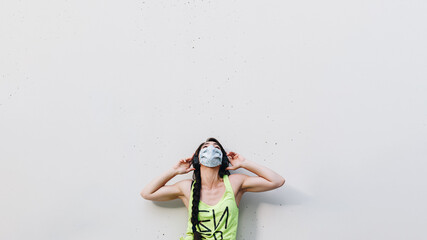 Isolated attractive young woman with face mask listening to music with her headphones on the street.