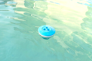 Blue chlorine dispenser floating in a home pool, cleaning and care of the domestic pool.