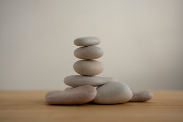 Fototapeta na wymiar One simplicity stones cairn isolated on white background, group of light gray pebbles built in tower, wood table