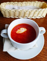 A white ceramic bowl of borscht and a bread basket on a brown wooden table