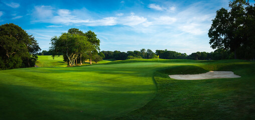 Panoramic landscape over the lush green fairway, the green, and the sand bunker at sundown - obrazy, fototapety, plakaty