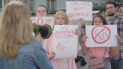 Crowd of people defending animal rights in urban city with blurred woman shouting through megaphone at front. Group of male and female eco-activists on demonstration.