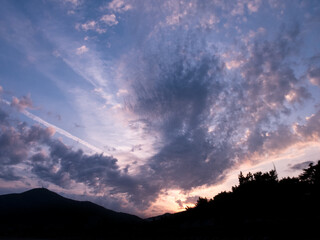 Evening sunset pink-purple sky with clouds over dark silhouette of mountains.