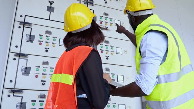 Electrical engineers checking control panel board with tablet. 