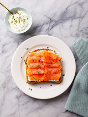 Sandwich, toast with smoked salmon and cream cheese on white plate. Marble background. Top view.