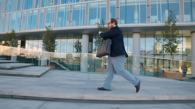 Side view of obese businessman running late for work checking time outdoors
