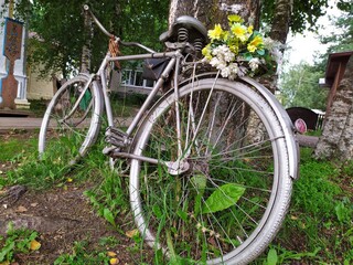 Fototapeta na wymiar An old metal grey bicycle with a bouquet of yellow flowers by a tree