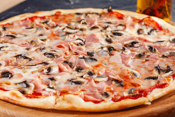 Pizza with ham and mushrooms on wooden board on dark background. Close-up