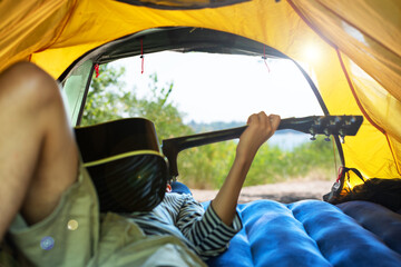 Teenage boy lying in tent playing guitar. Young man enjoying outdoor recreation near river. Camping. Summer vacation. Local tourism concept. View from the inside of tent.