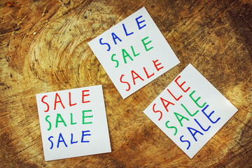 The word sale in three fonts and three colors on three small pieces of paper on a beautiful brown wood surface