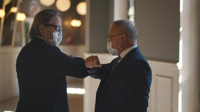 Mature Entrepreneurs In Medical Mask Greeting Touching Elbows