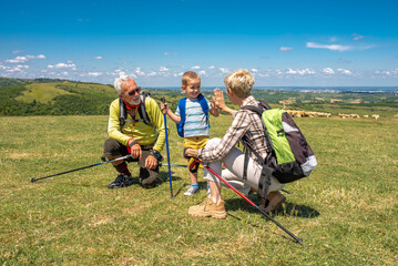 Family on outdoor adventure, grandparents and grandchild climbing hill on hike through countryside.