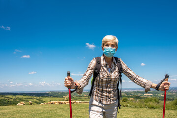 Active Caucasian senior woman wearing medical face mask while hiking in high mountains 