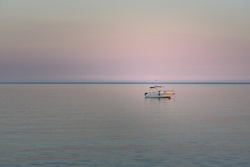 In the evening at sunset a small white boat in Italy is on the calm sea and small waves