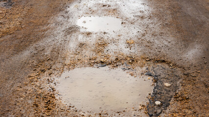 Bad road. Pits, potholes and puddles after rain on paved road. Background is an old road with cracked asphalt, gravel and sand