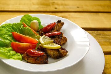 White plate with slices of grilled meat with lemon and tomato decorated.