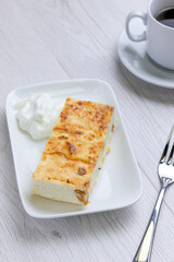 Dessert with cup of coffee on background. Cheese dessert on white plate on white wood table. Delicious breakfast in cafe. Home made bakery.