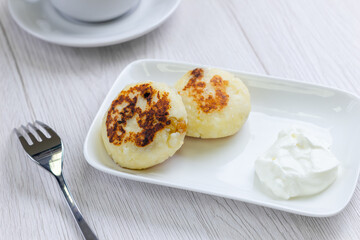 Dessert with cup of coffee on background. Cheese dessert on white plate on white wood table. Delicious breakfast in cafe. Home made bakery.