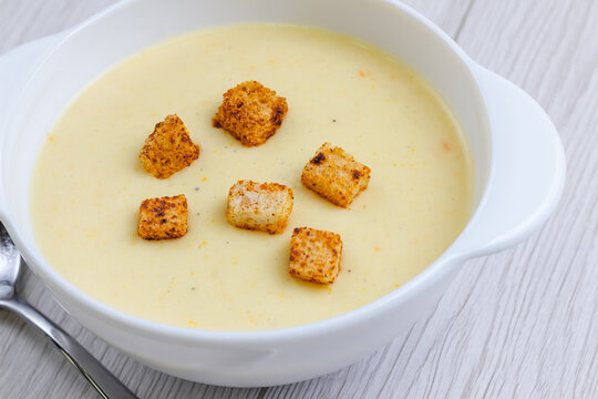 Cheese cream soup with snall toasts crutoons in white pottery on white wood table. Selective focus. Copy space