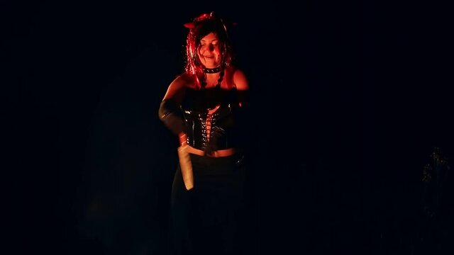 A woman in the form of a devil with horns at night by the fire with a knife dances a ritual dance