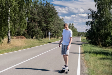 Young adult man skateboards on asphalt against forest and blue sky