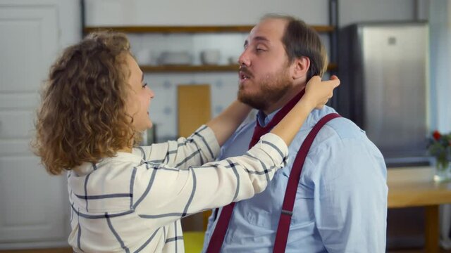 Beautiful wife tying red necktie to her overweight husband at home