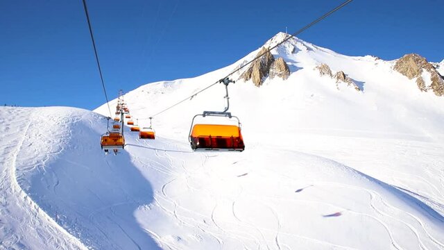 Ski lift ropeway on hilghland alpine mountain winter resort on bright sunny day. Ski chairlift cable way with people enjoy skiing and snowboarding. Scenic panoramic wide view of downhill slopes