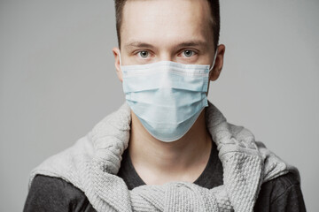 portrait of a young man in a blue mask looking at the camera. grey t-shirt, grey background. a protective agent against the pandemic face.