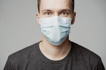 portrait of a young man in a mask looking into the camera. grey t-shirt and background. a protective agent against the pandemic face. fashionable hairstyle.