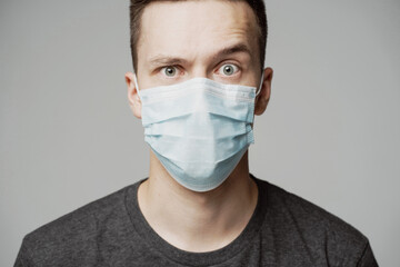 portrait of a young man in a mask looking into the camera. grey t-shirt and background. a protective agent against the pandemic face.