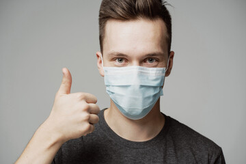 the young man points his finger at the top, a gesture well cool. portrait of a guy in a blue mask, protecting from the covad-19 pandemic. calm mood, looking at the camera