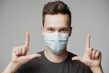 confident man, makes a gesture of two hands fingers on top. portrait of a young man in a blue mask that protects against the covid-19 pandemic. a friend shows where the camera is looking