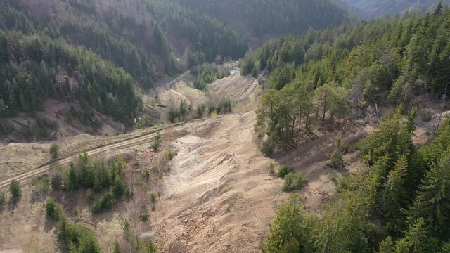 Flight above former copper surface mine in mountains, surrounded by mostly coniferous forest. First snow flakes in air visible, winter season. 
