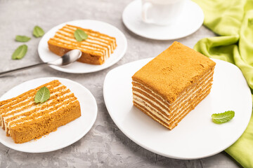 Homemade honey cake with milk cream and mint with cup of coffee on a gray concrete background. Side view, selective focus.