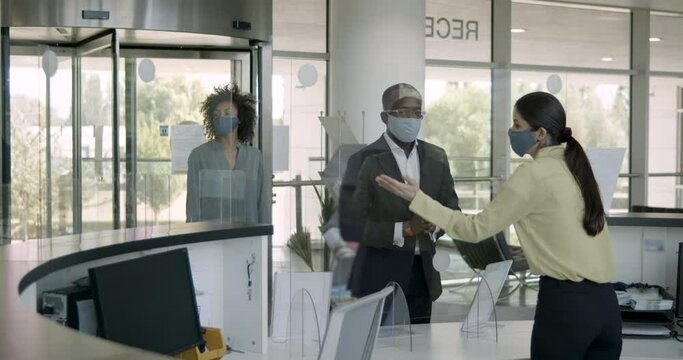 Business people arriving in corporate office lobby wearing protective face mask, receptionist giving them directions