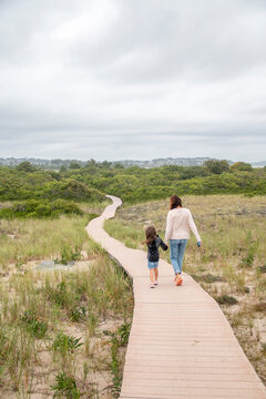 Mother and daughter walking down a wooden path to the beach