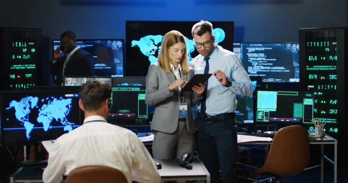 Caucasian male and female digital security analytics talking and using tablet device in monitoring military room. Colleagues man and woman discussing governmental surveillance in anti-terrorism center