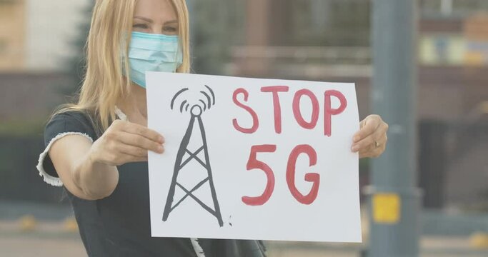 Confident woman in face mask stretching Stop 5G poster. Portrait of serious Caucasian eco-activist protesting against harmful impact of mobile towers causing Covid-19 pandemic. Cinema 4k ProRes HQ.