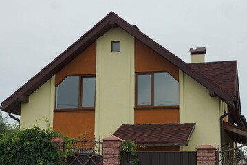 facade of a brown private house with two windows against a gray sky